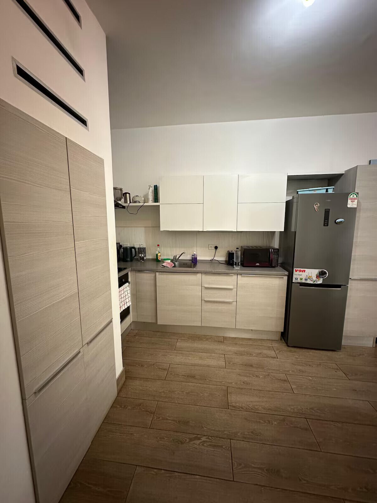 Una cocina con armarios de madera clara, un refrigerador de acero inoxidable y un microondas.