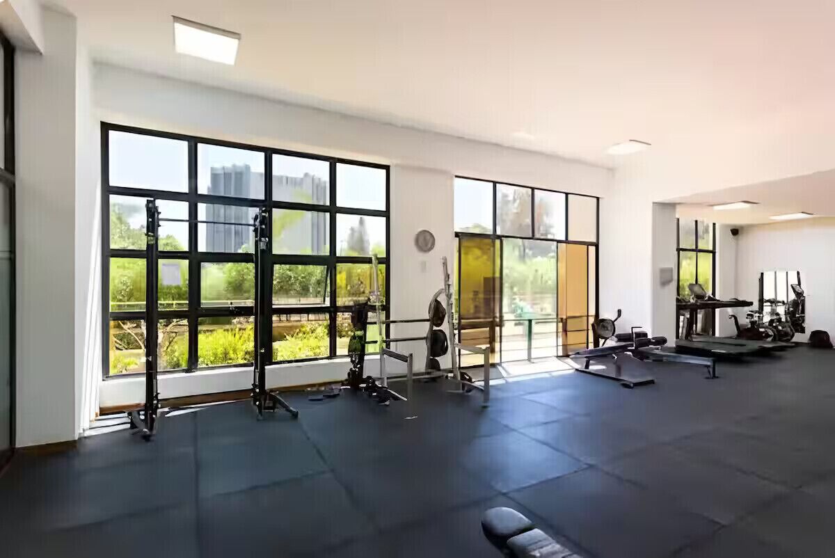 A gym with large windows, exercise equipment, and a clock on the wall.