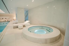 Ein moderner Wellnessbereich mit einer runden Whirlwanne, Liegestühlen und einem Pool.