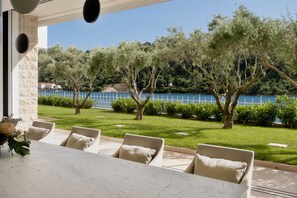 Eine Terrasse mit einem Marmortisch und -stühlen, mit Blick auf einen See und Bäume.