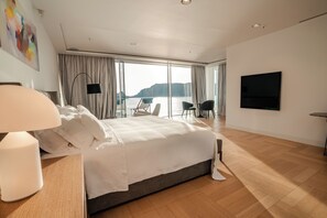 A modern hotel room with a large bed, a desk with a lamp, a flat-screen TV, and a view of the sea through large windows. - Luxury Villa Katino Estate with Private Pool & Sea Views (Šipanska Luka)