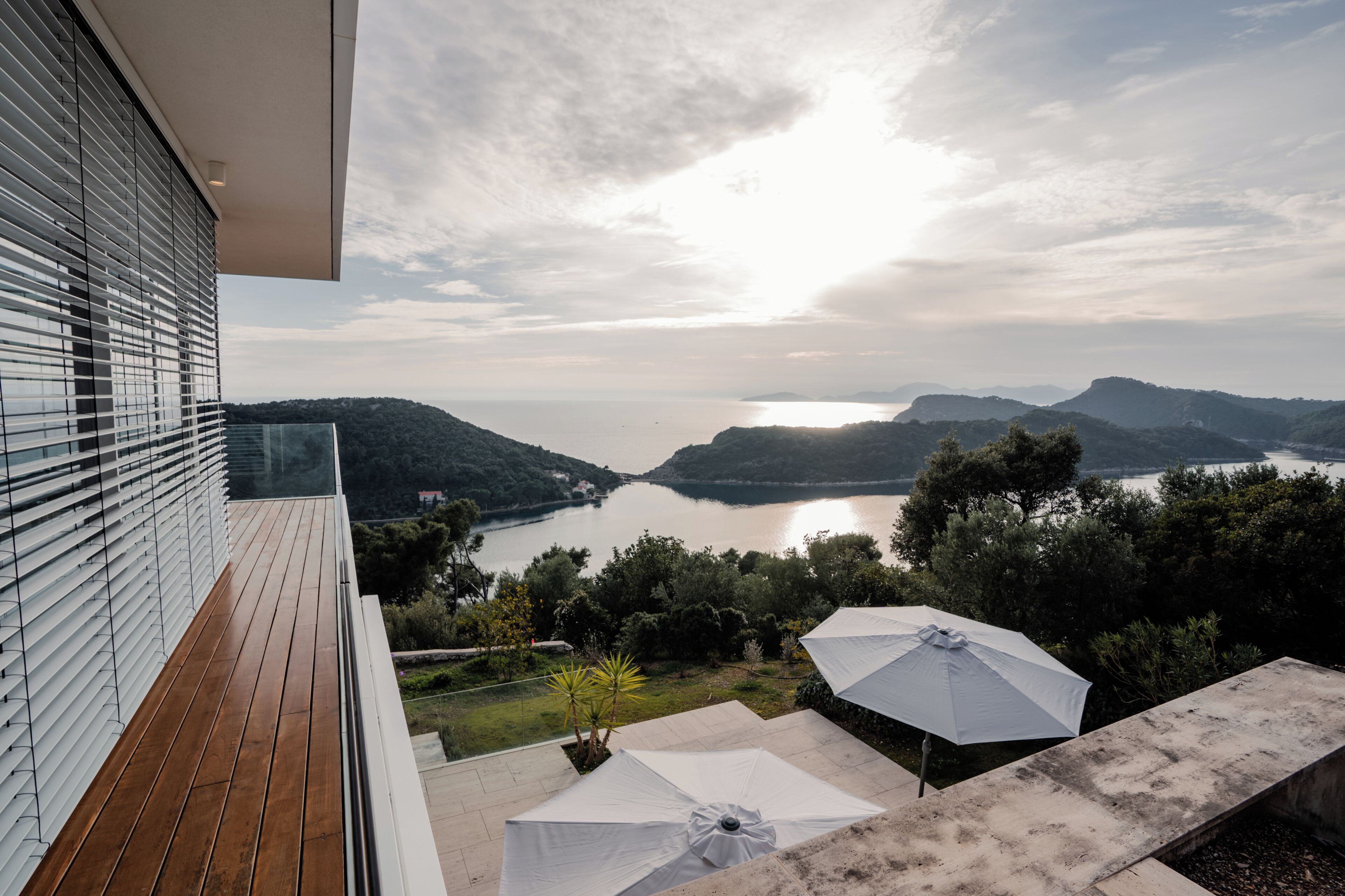 Un balcon avec vue sur un lac et des montagnes, une terrasse en bois et des parasols d’extérieur.
