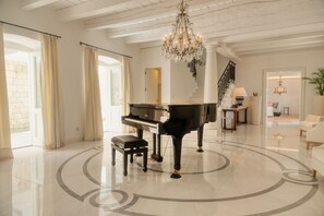 A grand piano in a spacious room with a chandelier, a staircase, and a view of a brick wall. - Luxury Villa Katino Estate with Private Pool & Sea Views (Šipanska Luka)