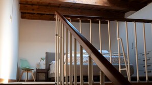 A room with a wooden ceiling, a bed, a chair, and a nightstand.