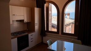 A compact kitchen with a gas stove, oven, and white cabinets. There is a dining table with chairs and a large window with a view of buildings.