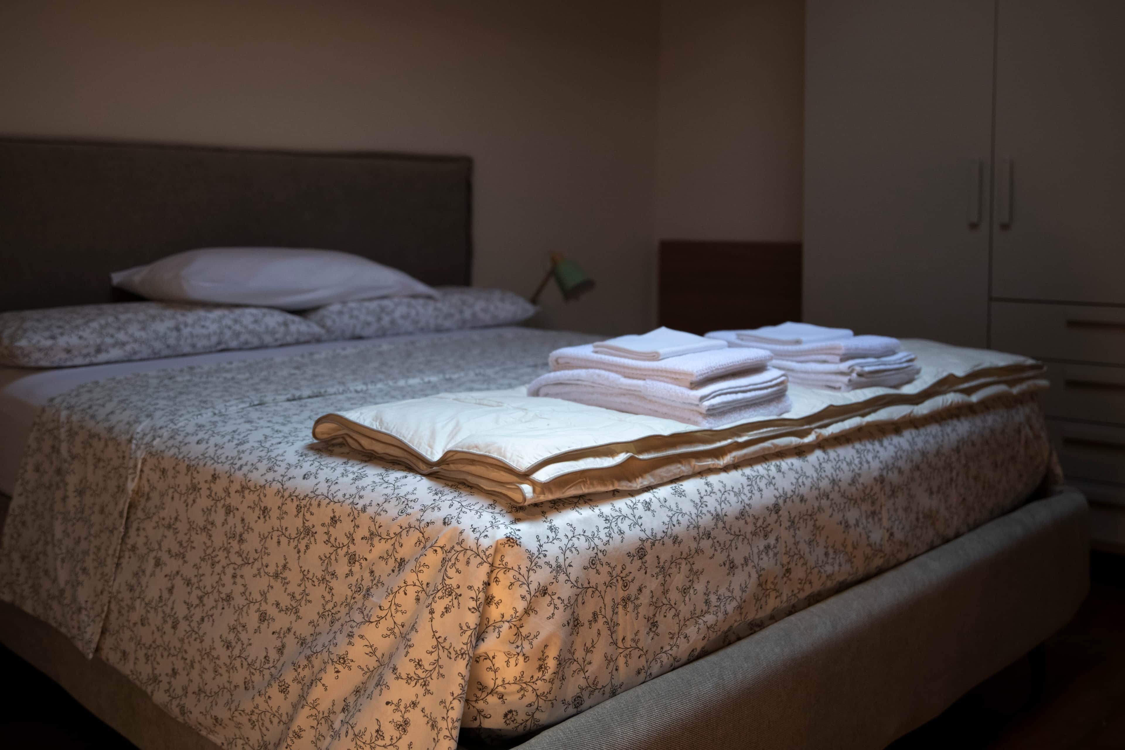 A neatly made bed with a floral-patterned bedspread and a folded white towel on top.