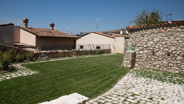 A courtyard with a paved walkway, a stone wall, and a grassy area.