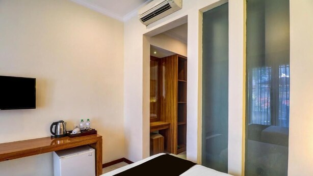 Une chambre d’hôtel comprenant un lit, un téléviseur fixé au mur, un petit bureau avec une bouilloire et une armoire.