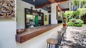 Un espace bar avec un comptoir et des tabourets en bois, un panneau décoratif mural et une vue sur un jardin luxuriant.