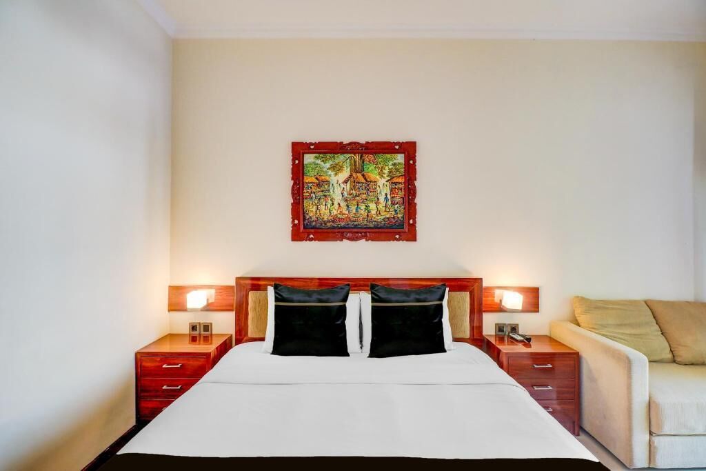 A hotel room with a bed, two bedside tables, a nightstand, a sofa, and a wall-mounted painting.