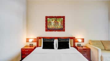 Una habitación de hotel con cama, dos mesitas de noche, un sofá y un cuadro colgado en la pared.