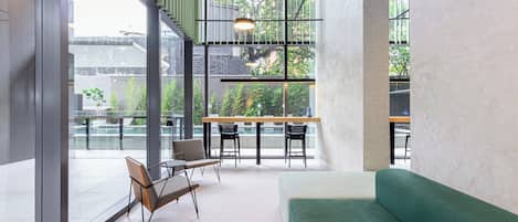 A modern interior with a green sofa, a dining area with a table and chairs, and large windows offering a view of greenery.