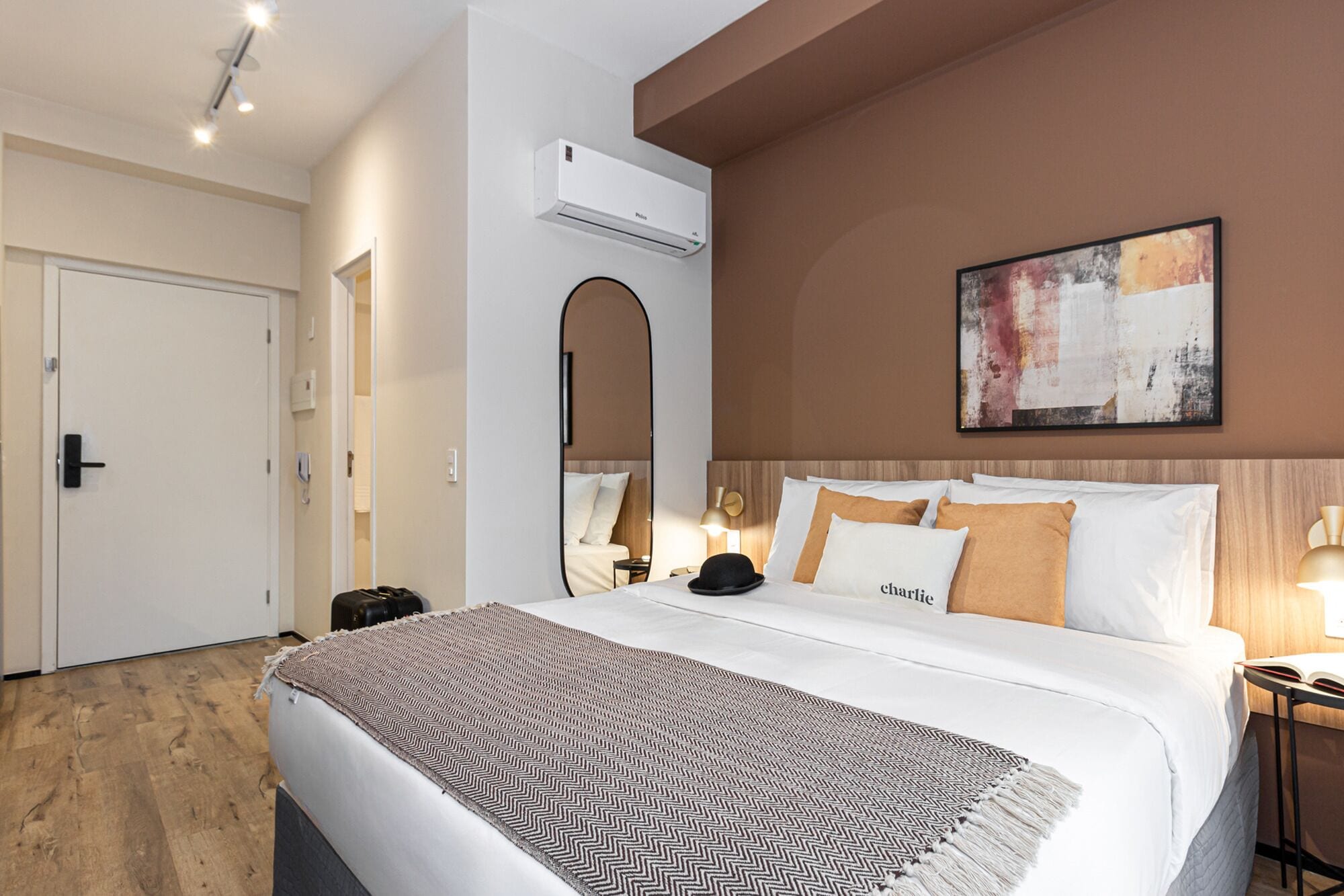 Quarto de hotel com cama, mesa de cabeceira, luminária e um quadro na parede.