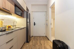 Cocina estrecha con refrigerador, microondas y pileta. Hay una maleta en el piso.