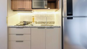 Een kleine keuken met een ingebouwde magnetron, een koelkast van roestvrij staal en een granieten aanrecht.