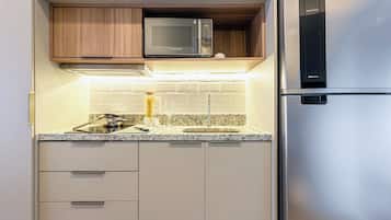 Una cocina compacta con microondas integrado, refrigerador de acero inoxidable y encimera de granito.