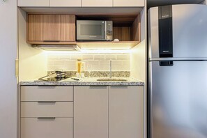 A compact kitchen with a built-in microwave, stainless steel refrigerator, and a granite countertop. - Charlie H.S Studios Pinheiros - Soft Opening (São Paulo)