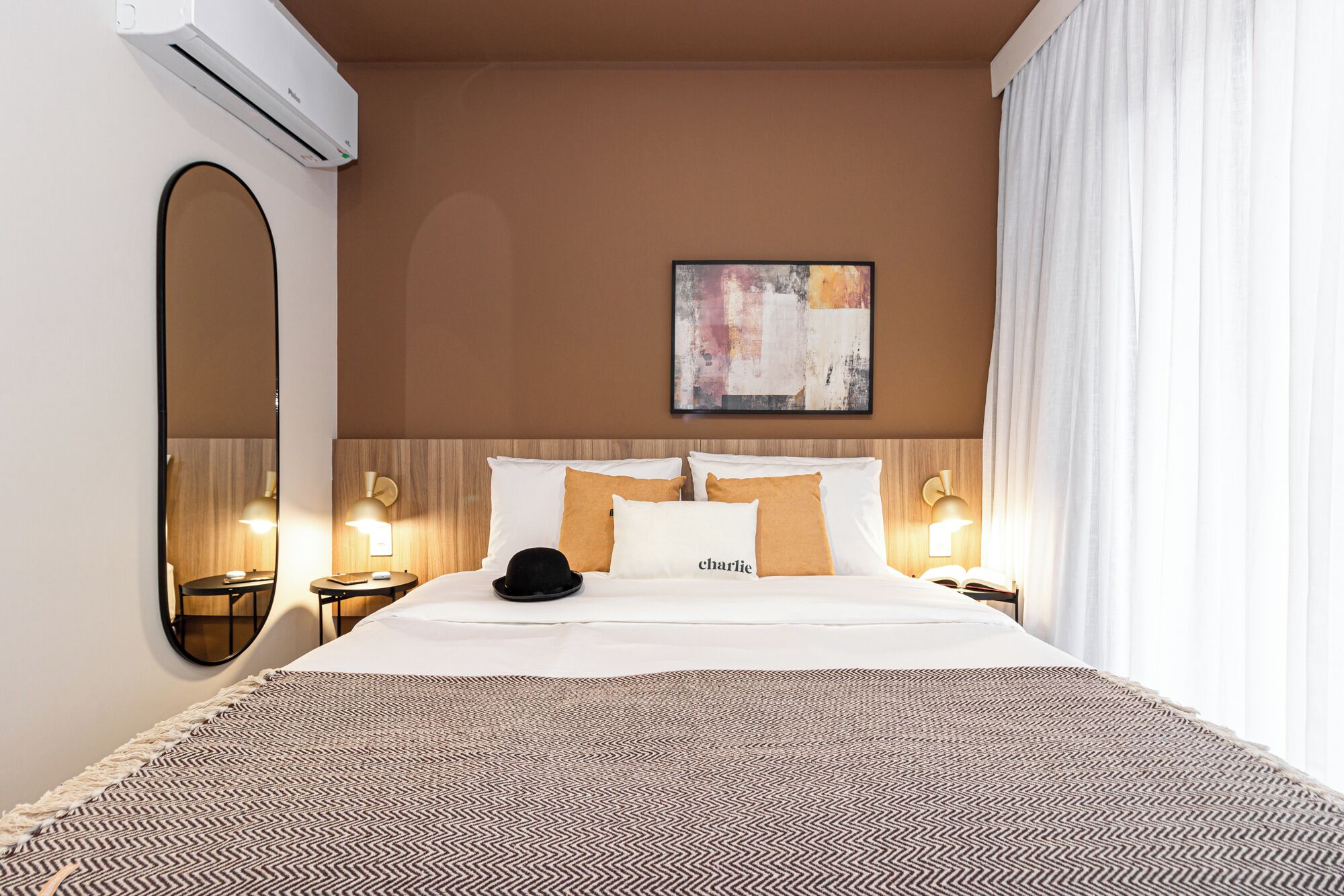 A hotel room with a bed, a bedside table, a lamp, a mirror, and a painting on the wall.