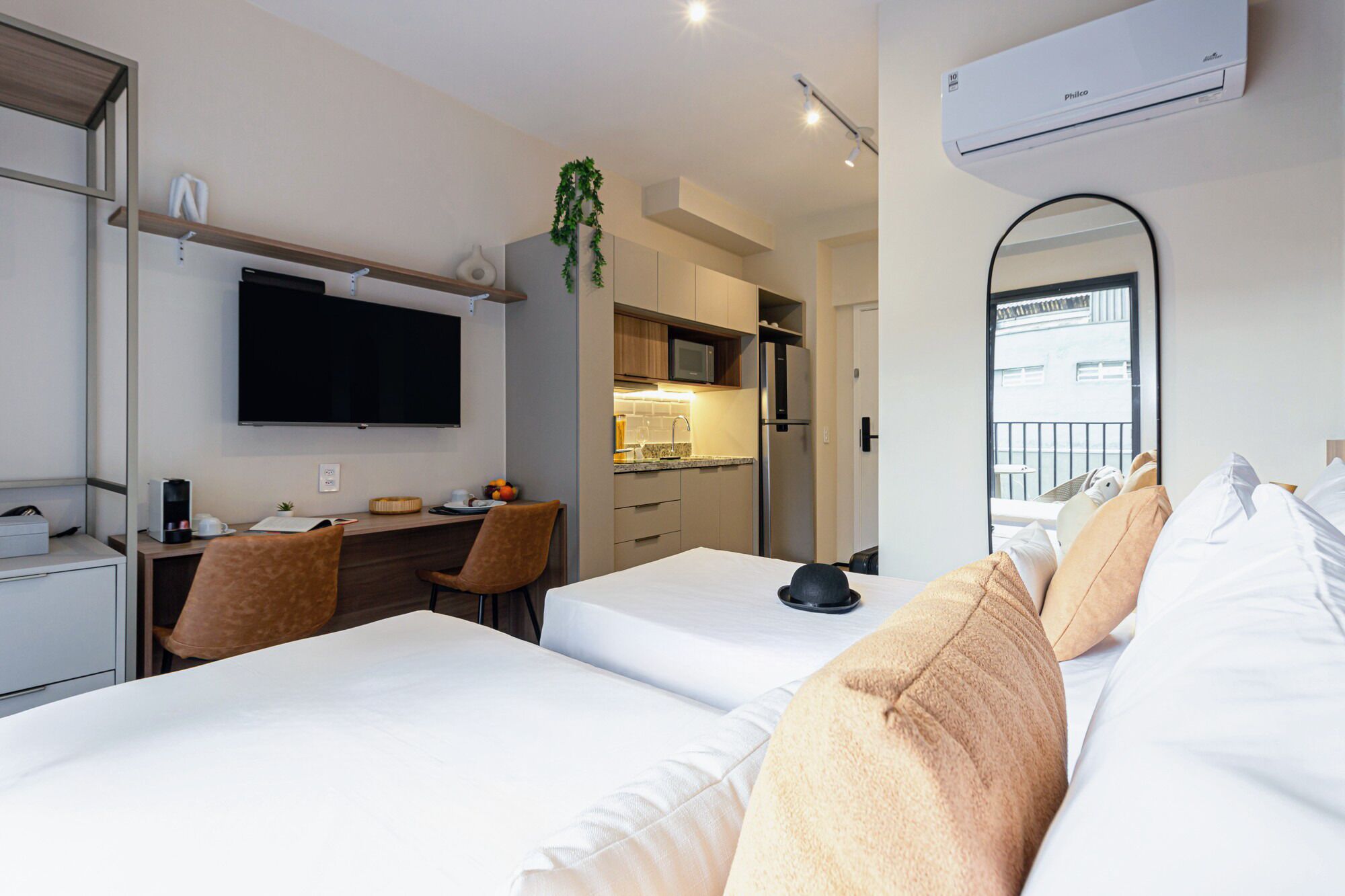 A hotel room with two beds, a desk, a TV, a minibar, and a balcony view.