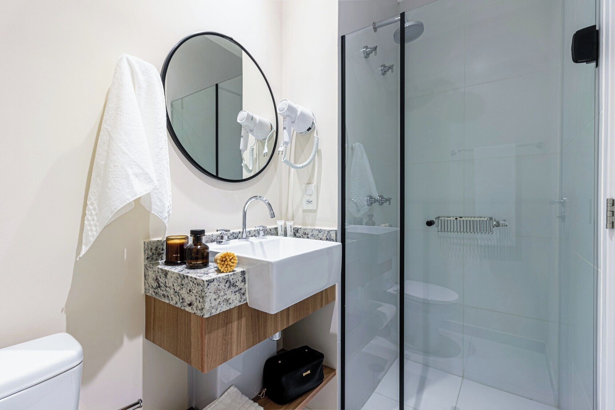 Un baño con lavabo, espejo, toalla y ducha con mampara de vidrio.