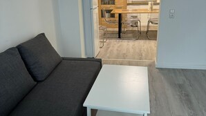Un salon moderne avec un canapé gris, une table basse blanche et un coin cuisine à l’arrière-plan.