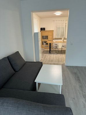 Ein modernes Wohnzimmer mit einer grauen Couch, einem weißen Couchtisch und einer Küchenzeile im Hintergrund.