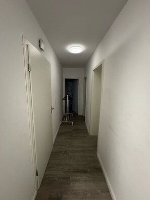 Ein schmaler Gang mit weißen Wänden und Holzdielen, der zu einer Tür am Ende führt.