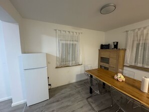 A compact kitchen with a white refrigerator, a wooden dining table, and a coffee maker on the counter.