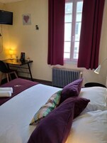 Una habitación de hotel con cama, escritorio, silla, radiador y ventana con cortinas.