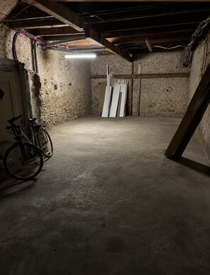 Ein spärlich beleuchteter Dachbodenraum mit freiliegenden Holzbalken, einem Fahrrad und mehreren an der Wand angelehnten weißen Tafeln.