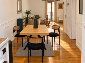 A dining area with a wooden table and four chairs, a sofa, a potted plant, and a small round table with a vase. - Rose des Orpellières – Terrace, A/C and shared garage (Sérignan)