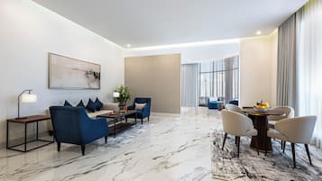 Et moderne hotelværelse med marmorgulv, en sofa, et spisebord med stole, et sofabord og et stort vindue med gardiner.