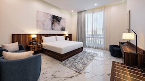 A hotel room with a bed, a desk, a chair, a nightstand, a painting, and a view of the outdoors.