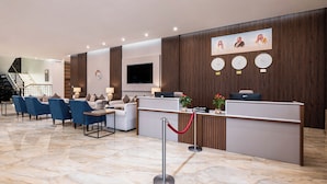 A hotel reception area with a reception desk, seating area, and a staircase.