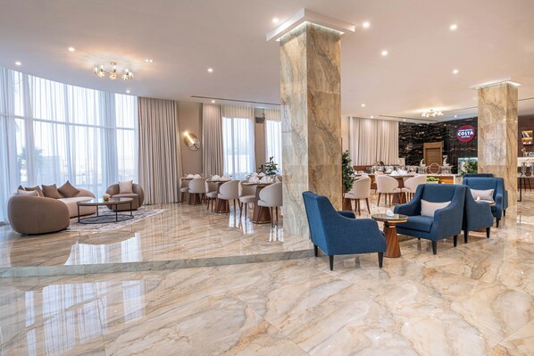 Un hall d’entrée spacieux avec un sol en marbre, des coins salon et un bar à café.