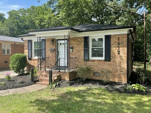 A two-story house with a brick facade, black shutters, and a front porch with a staircase. - Renovated Brick Cottage · 10 Min to Uptown (Charlotte)