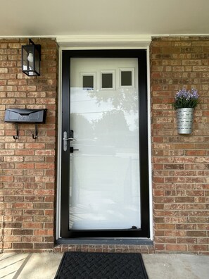A front door with a mailbox, a potted plant, and a wall-mounted light fixture. - Renovated Brick Cottage · 10 Min to Uptown (Charlotte)