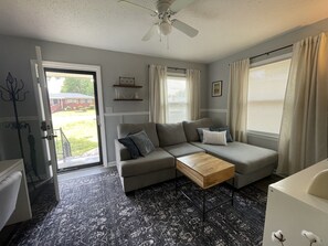 A living room with a grey sofa, a wooden coffee table, and a ceiling fan. - Renovated Brick Cottage · 10 Min to Uptown (Charlotte)
