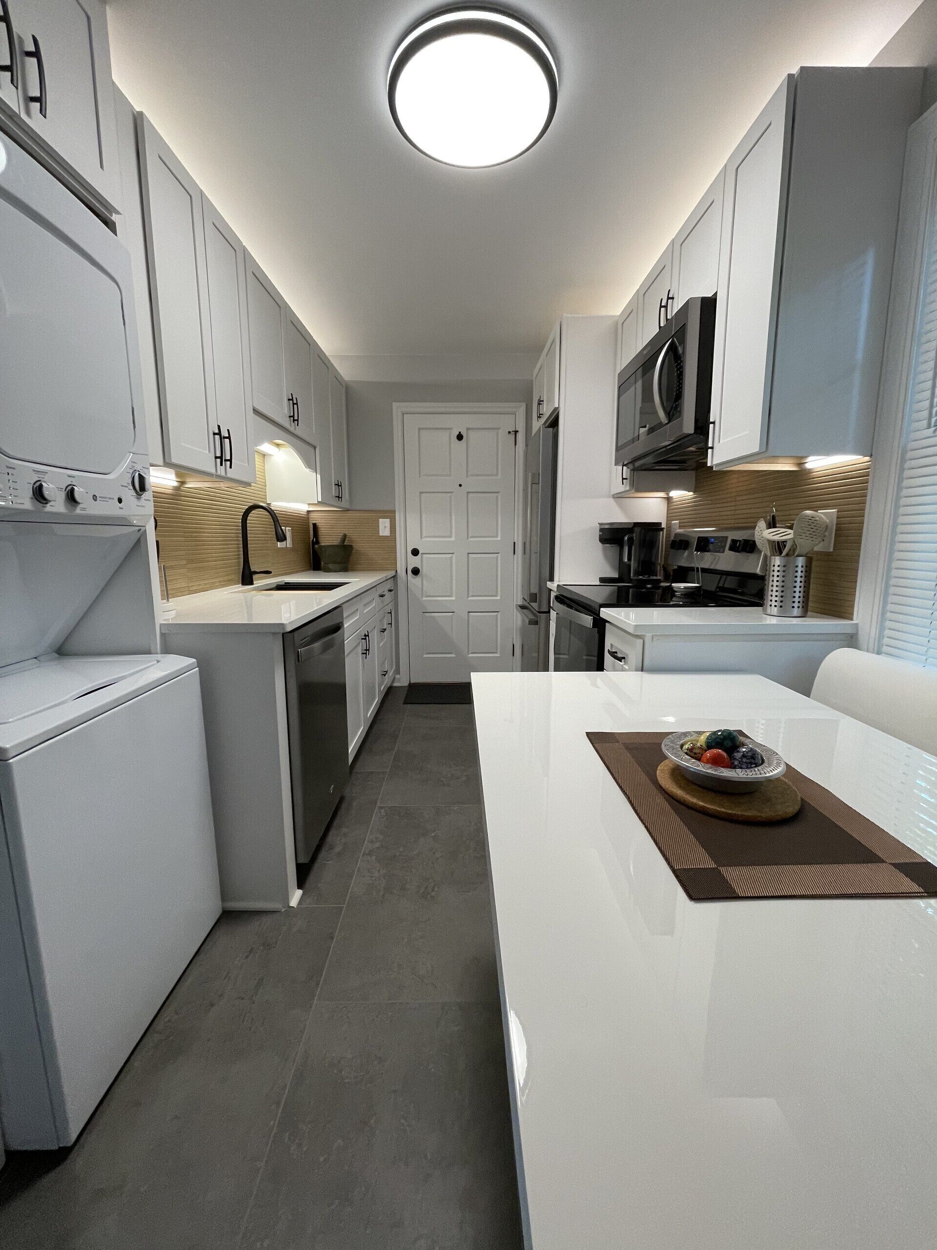 A modern kitchen with white cabinetry, a central island, and a microwave above the stove.