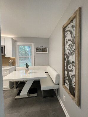 Eine moderne Küche mit weißen Schränken, einem Esstisch mit Bänken und einem dekorativen Metallbaum an der Wand.