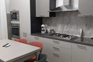 A modern kitchen with built-in appliances, a dining area with two chairs, and a marble backsplash.