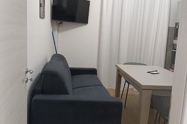 A small room with a sofa, a table, a flat-screen TV mounted on the wall, and a curtain.