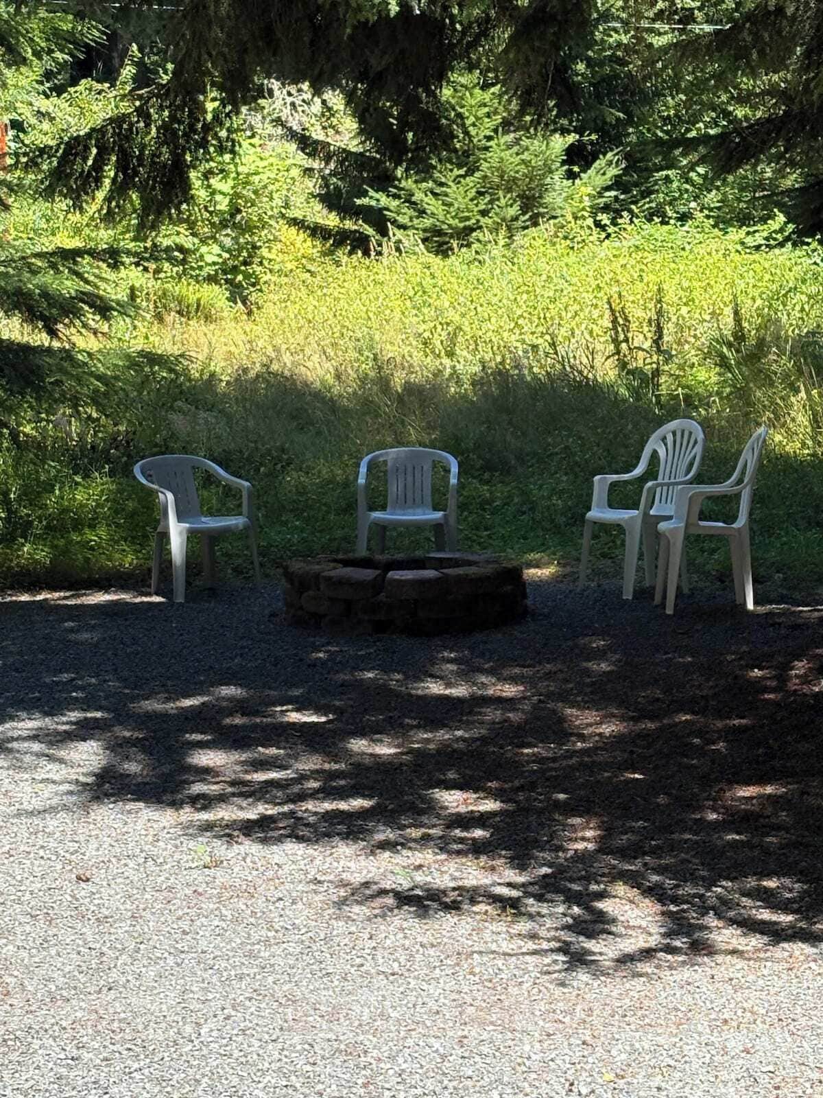 Un área de grava con tres sillas de plástico blanco y un hogar de piedra.