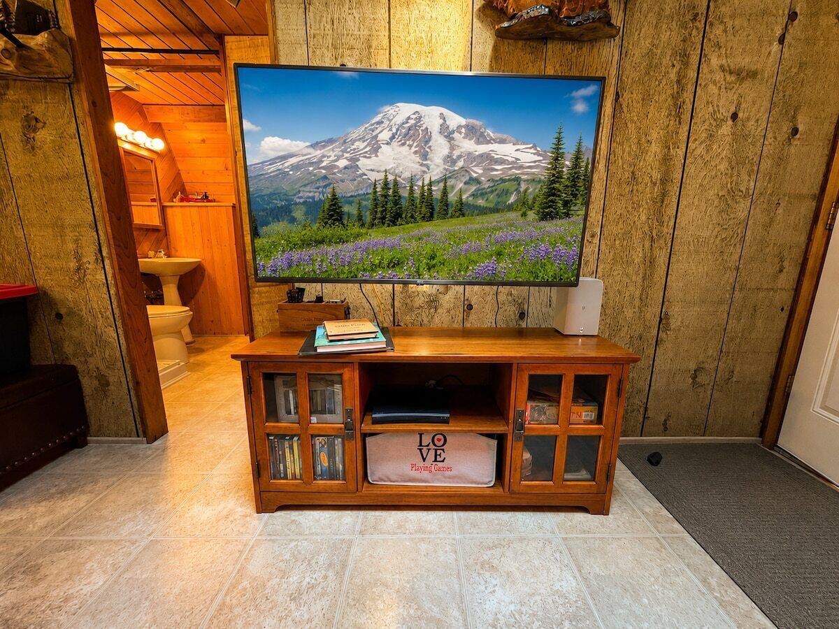 A wooden entertainment center with a television displaying a mountain landscape, a small shelf with books, and a storage bin labeled 'LOVE Playing Games'.