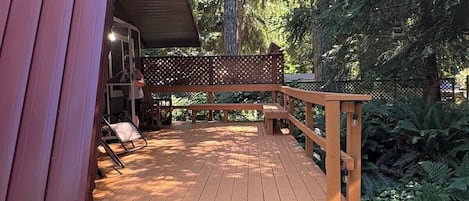 A wooden deck with a railing, leading to a covered area with a bench and a table.