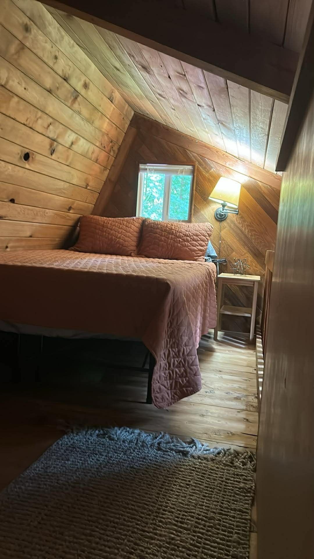 A cozy attic bedroom with a bed, a lamp, and a window.