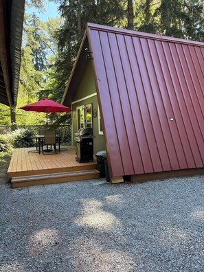 Uma cabana pequena com um deck de madeira e um guarda-sol vermelho.