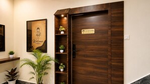 A reception area with a wooden door, a welcome poster, potted plants, and a marble floor.