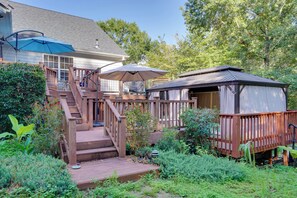 A wooden deck with a staircase leading to a covered area, surrounded by lush greenery. - Hot Tub & Deck! Loganville Group Retreat (Loganville)