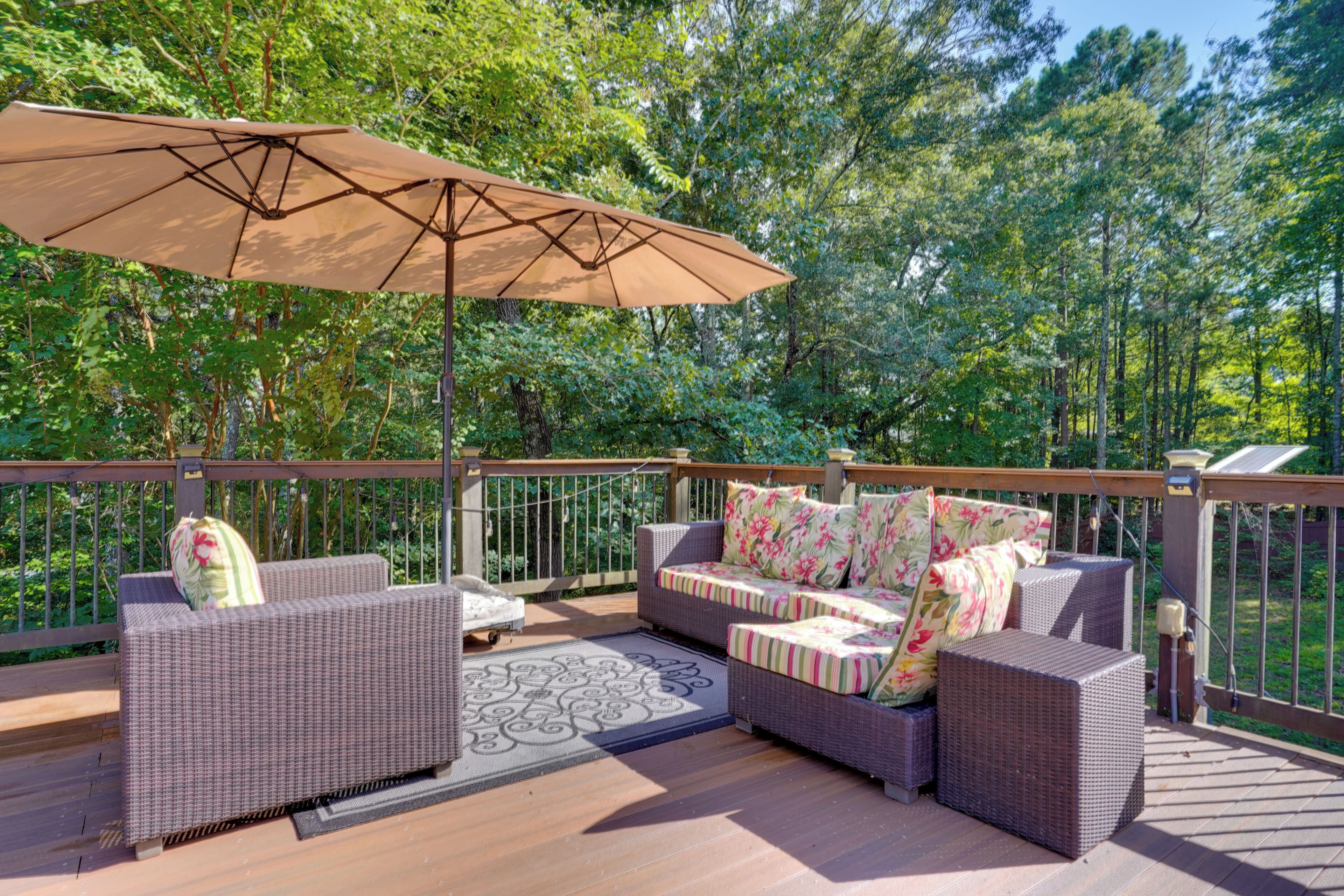 A deck with wicker furniture, a patterned rug, and a large umbrella.